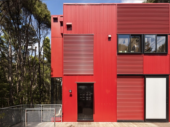 Su exterior rojo brillante del revestimiento del hierro acanalado ciertamente le hace estallido contra los alrededores del arbusto verde