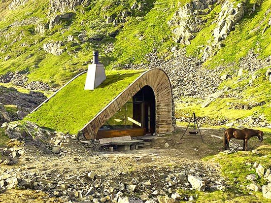 La cabina minúscula imponente se coloca a lo largo de un lago, entre altos picos noruegos.